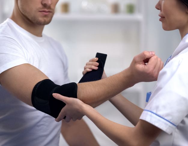 Zakładanie ortezy stabilizującej staw łokciowy podczas czynności rehabilitacyjnych.
